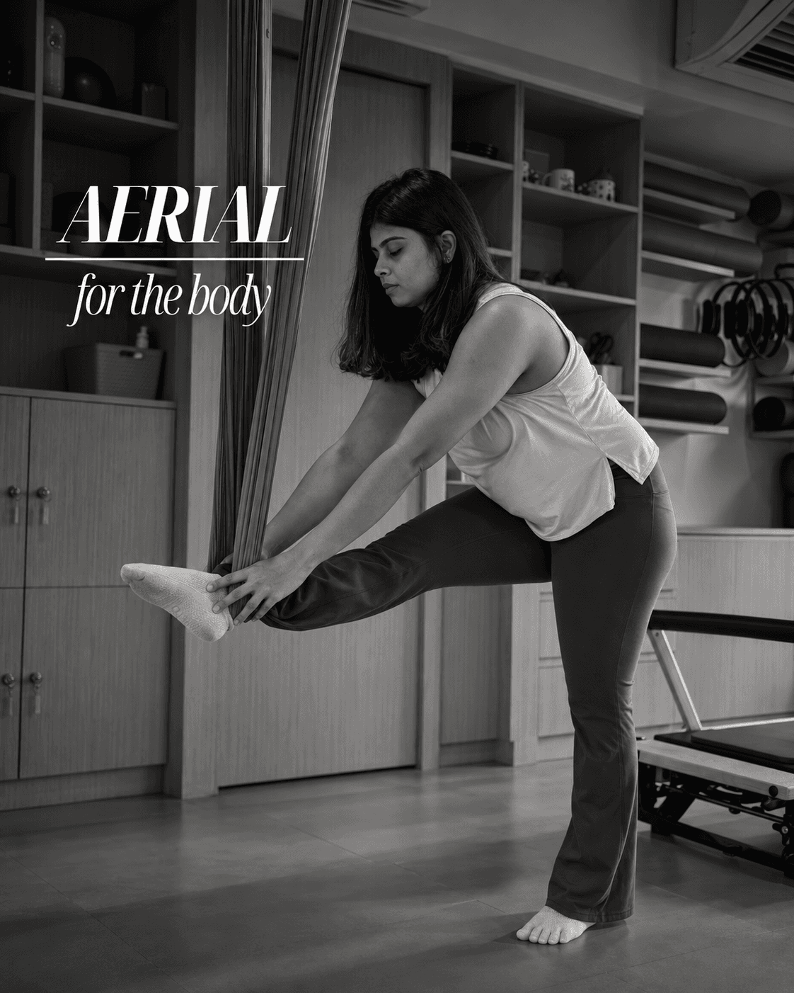 Black-and-white photo of a woman stretching one leg out in a studio, captioned "Aerial — for the body".